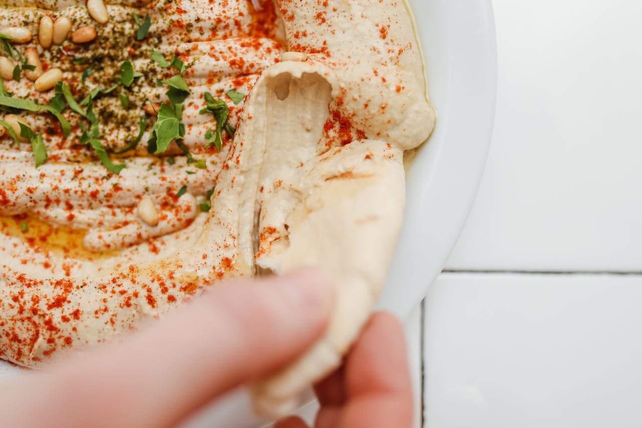 Delicious hummus with spices and a piece of pita bread being dipped, perfect for food lovers.